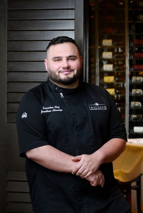 Headshot of Chef Jonathan Abrevaya in the dining room in front of a wooden shutter style door with a wine wall in the background