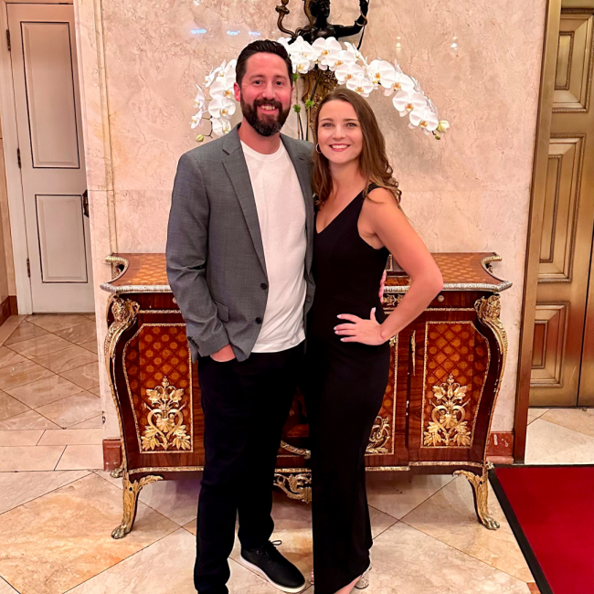 Chris and Karen in dressed up attire in front of a credenza at a hotel.