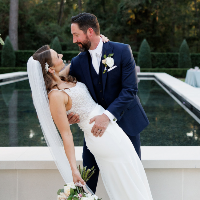 Karen and Chris in wedding attire posed in a dip pose staring into each others eyes in front of a large reflecting pool