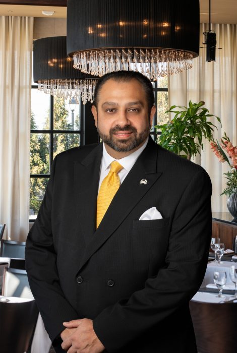 headshot of general manager Blake Goldie standing int eh dining room in a dark suite with yellow tie, crab lapel pin and white satin pocket square