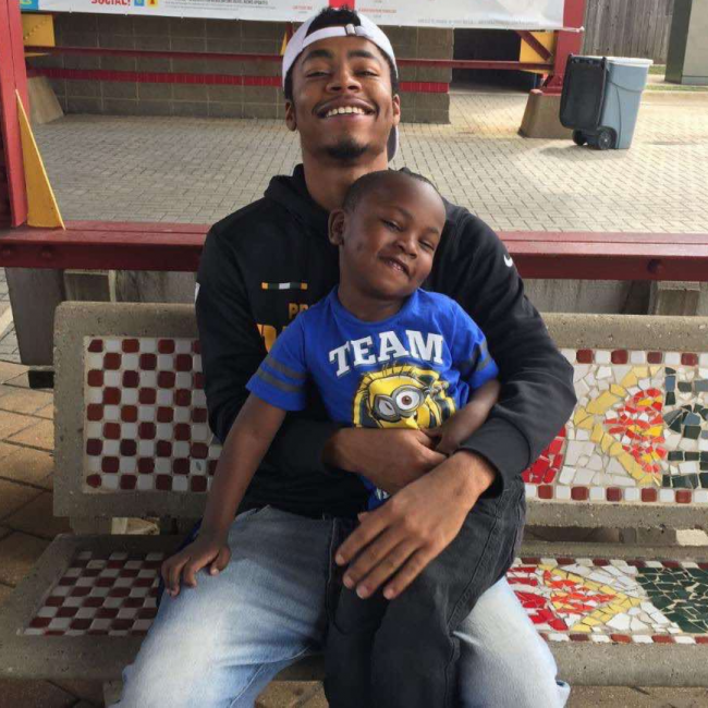 Chef Dom of Truluck's Arboretum with his son sitting on a tiled bench. His son is sitting in his lap and bother are smiling big.