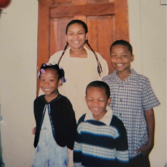 Chef Dom as as a young kid with his 3 siblings standing in from of a door and smiling