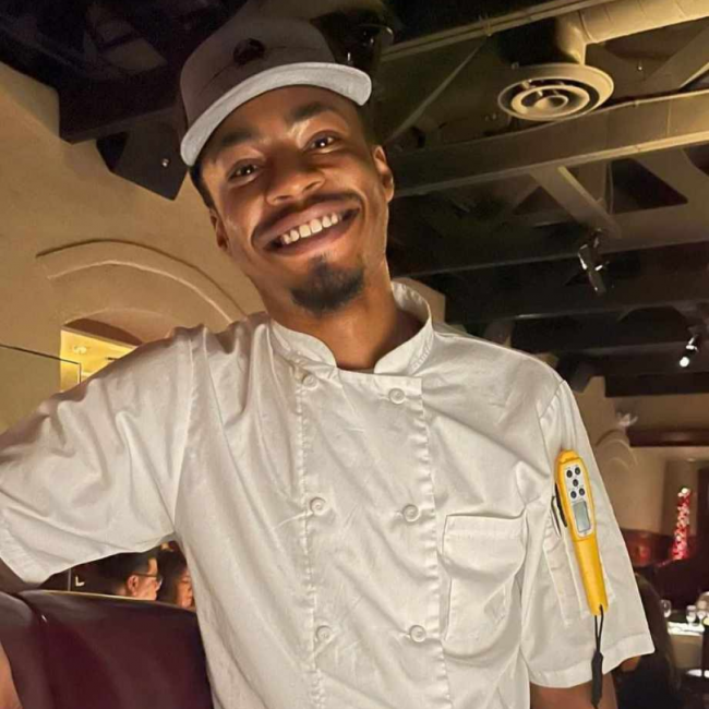 Chef Dom in his Truluck's ball cap and chef coat standing at a booth in the Arboretum dining room.