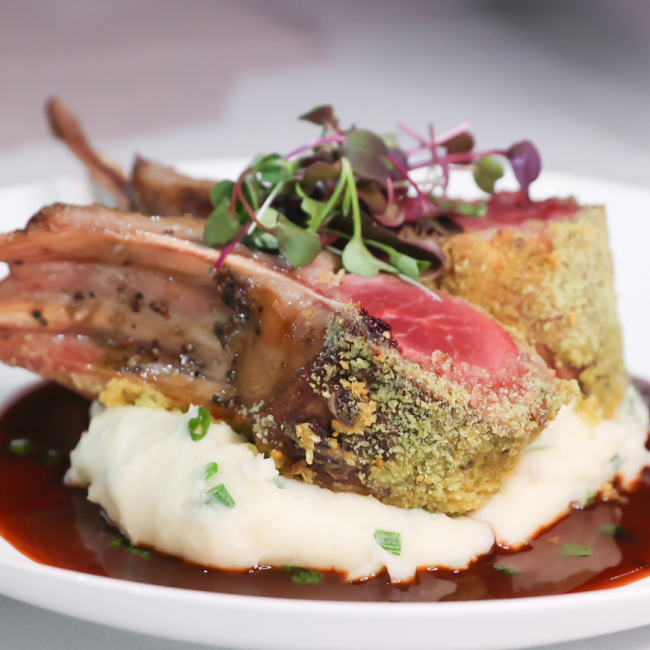 close up image of Lumina lamb chops crusted in dijon, parmesan cheese and herbs on a bed of parmesan mashed potatoes sitting in a rosemary shallot glaze and garnished with microgreens