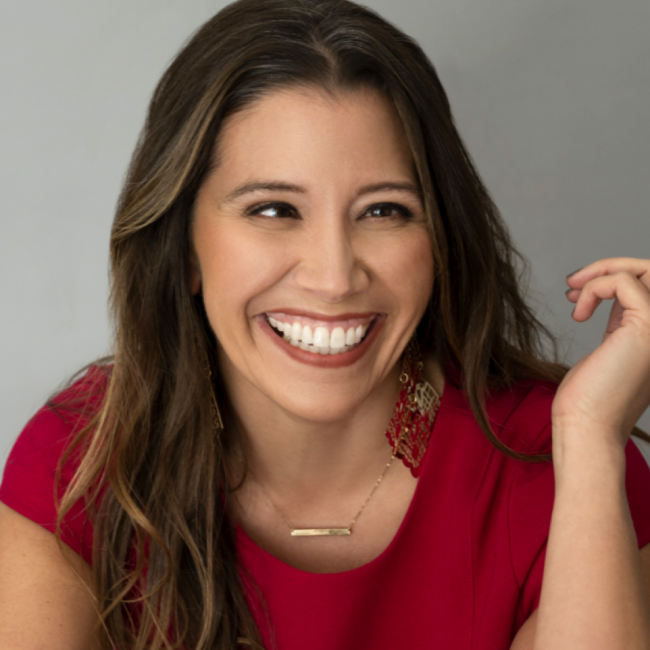 Amber Scheer CPCE sales & events manager and corporate trainer smiling in a red dress against a gray backdrop