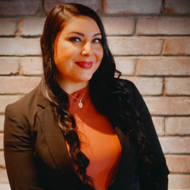 HEADSHOT of Brooke Torrez beverage manager of Truluck's Naples in an orange blouse with black suite jacket smiling in front of a wall.