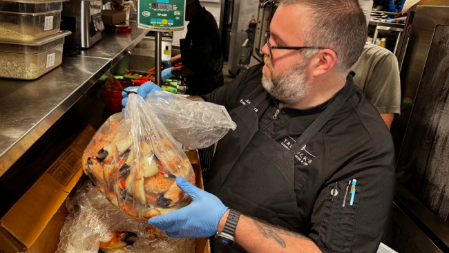 Chef Joe Mora in a black chef coat on the line unboxing fresh Florida stone crab