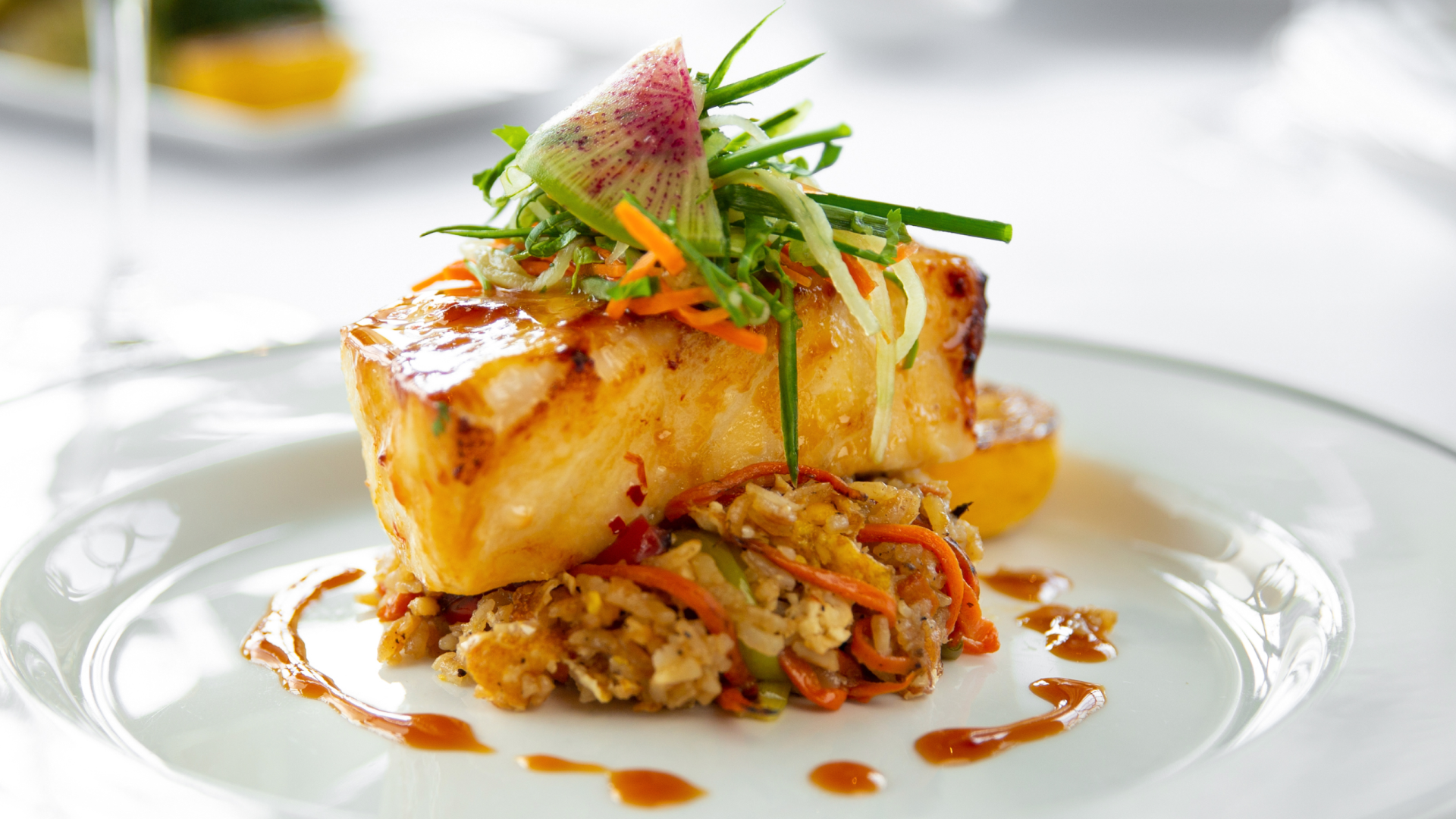 miso glazed seabass filet topped with chilled cucumber slaw topped with a watermelon radish over crab fried rice with sauce drizzled on the plate