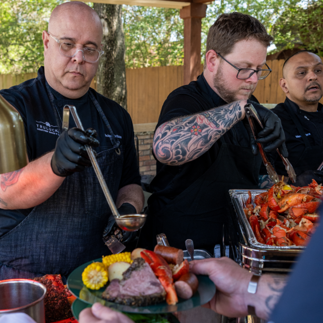 Chef Thomas, Chef Shane and Chef Manny serving lobster boil and prime rib in a buffet line to guests