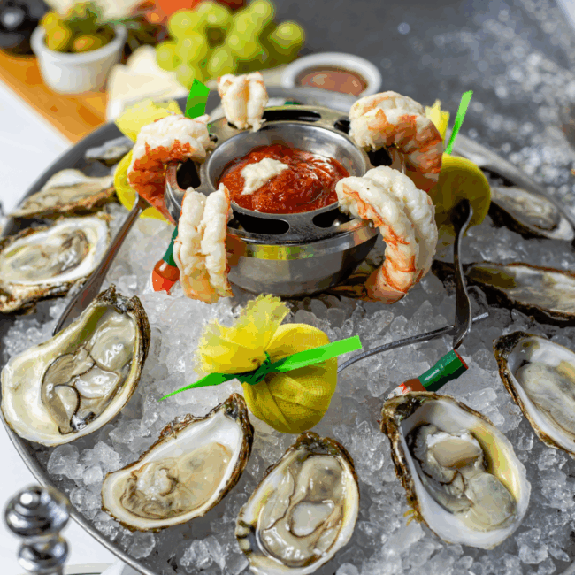 fresh shrimp and oysters on a large silver platter filled with crushed ice, mini tabasco bottles, lemon wraps and cocktail sauce