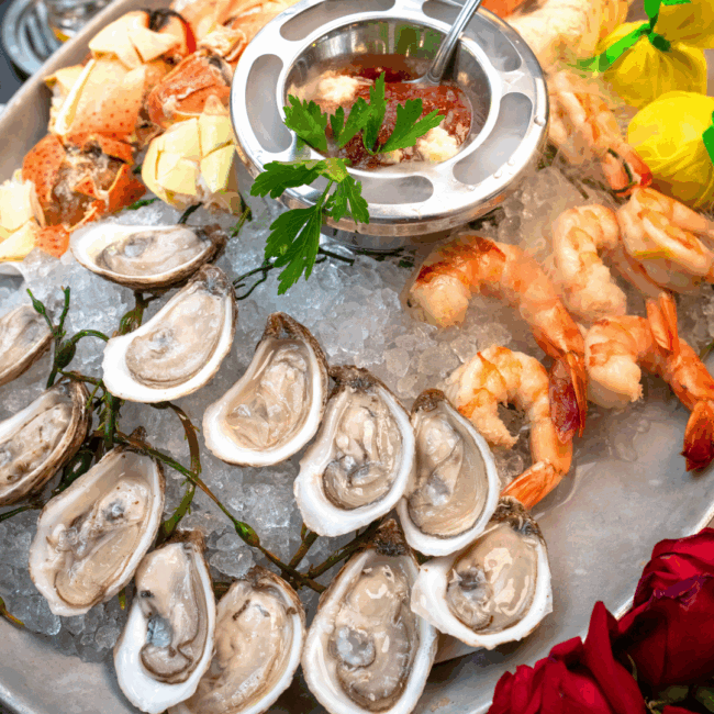a seafood platter filed with fresh shucked oysters on the half shell, cocktail shrimp, stone crab, a silver bowl with cocktails sauce, dollops of horseradish and fresh parsley with wrapped lemon halves