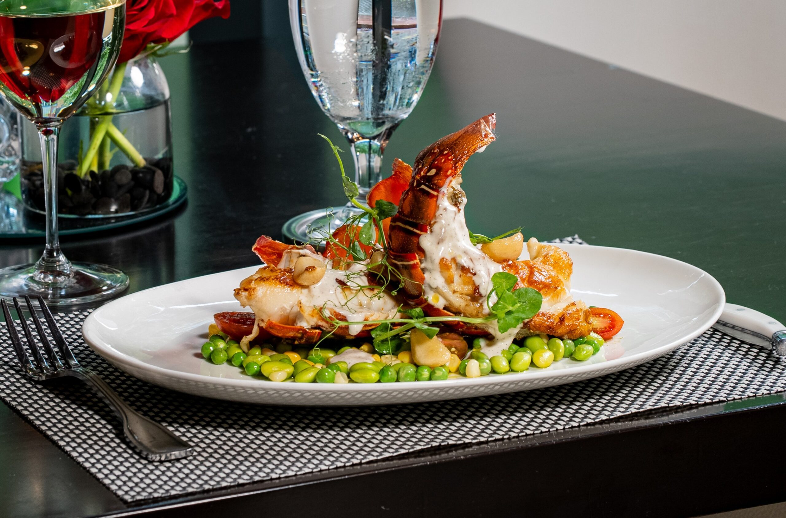 buttery lobster tails drizzled in melted brie with a summer succotash on a white china plate