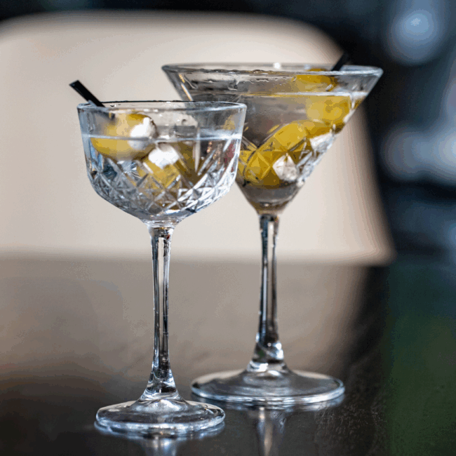 a tiny tini and regular sized dinner martini in chilled crystal stemmed glassware with blue cheese stuffed olives in each glass