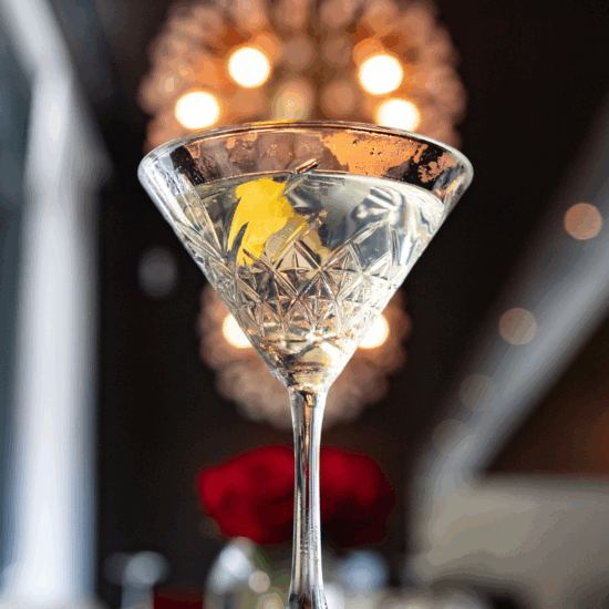 Bon Ton Martini in a crystal martini glass with a lemon twist garnish and a chandelier blurred in the background