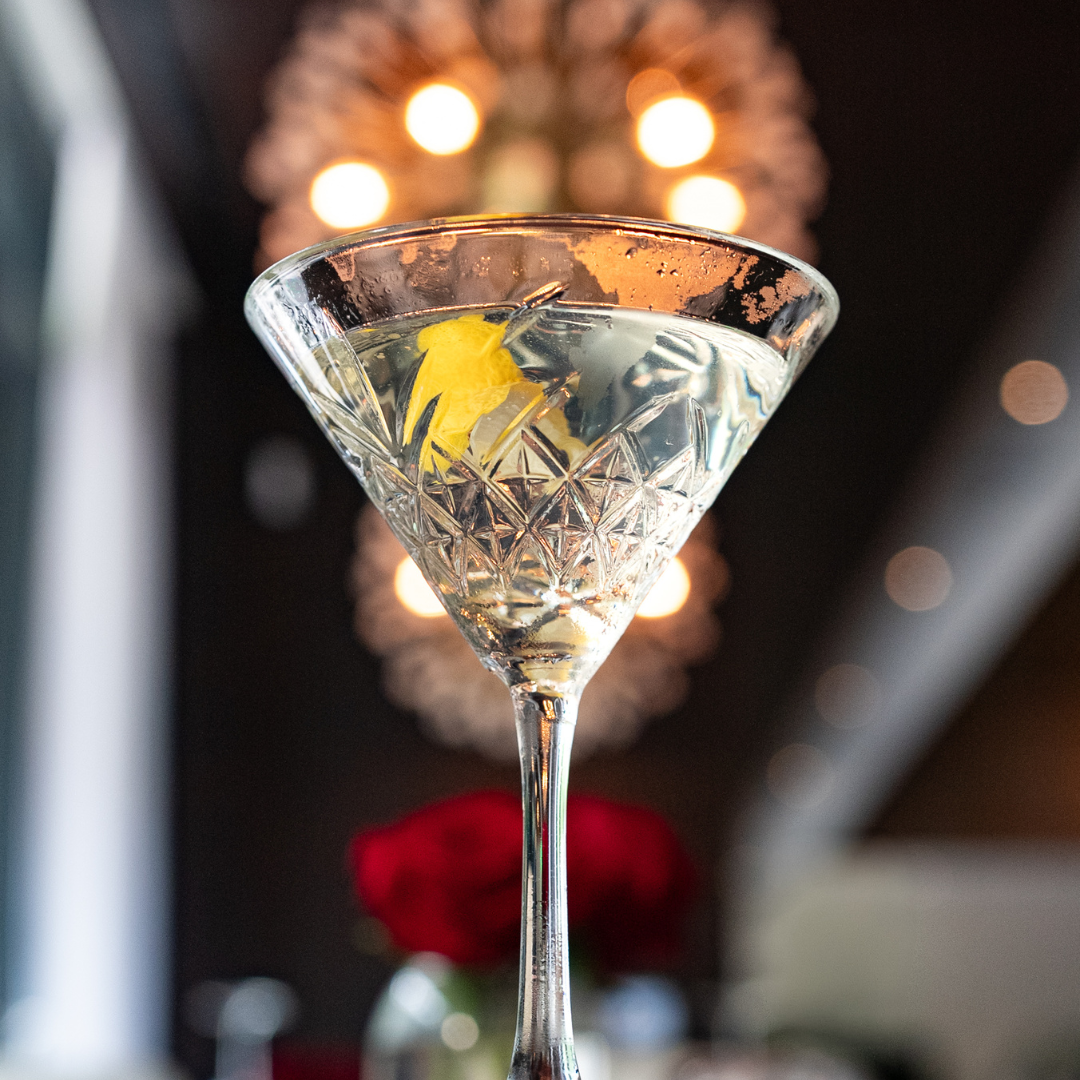Bon Ton Martini in a crystal martini glass with a lemon twist garnish and a chandelier blurred in the background
