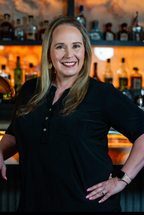 headshot of Misty Montague of Truluck's Austin in a black blouse posing in front of the bar top with one arm on the bartop and one hand on her hip