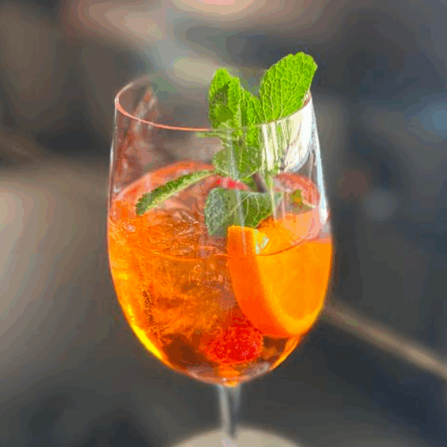 Elderflower spritz cocktail over ice in a wine glass with fresh mint, orange half wheel and raspberry