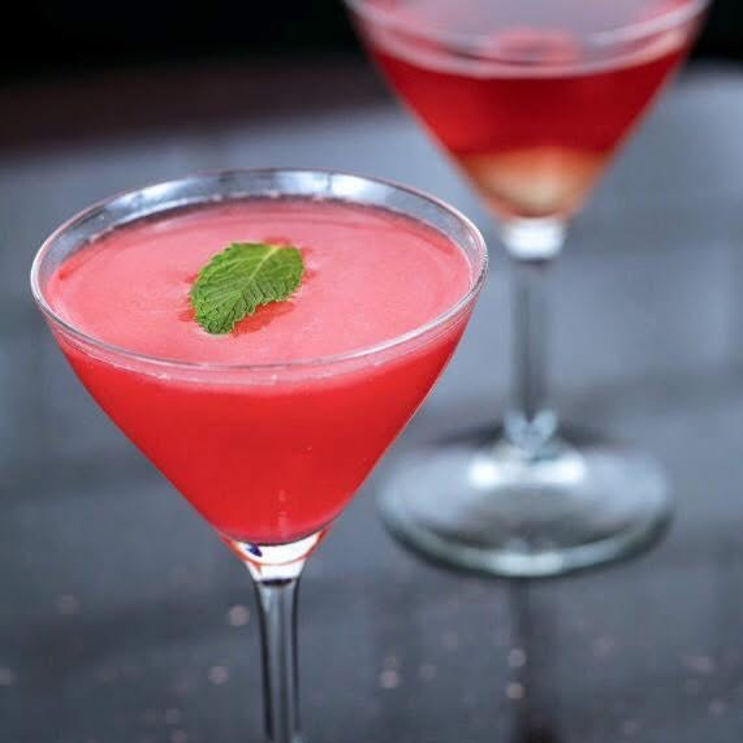 Red door martini in a bright red color topped with a mint leaf and served in a chilled martini glass