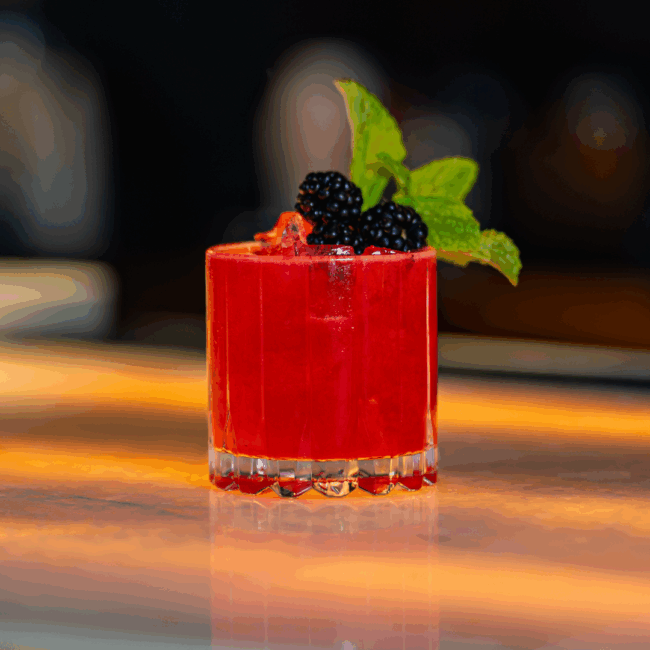 spicy blackberry margarita in a bright red pink hue topped with fresh blackberries and mint and served over ice in a rocks glass