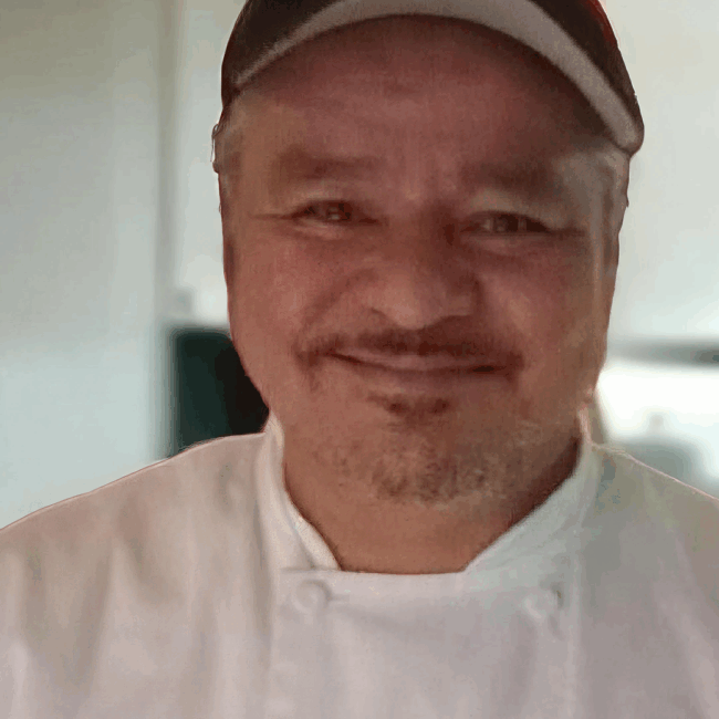 Up close photo of Rey Resendez smiling in a white chef coat and black ball cap