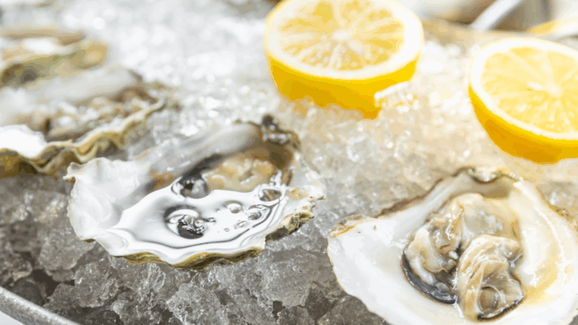 fresh shucked oysters on the half shell on a bed of ice with fresh lemon halves in the ice in the background