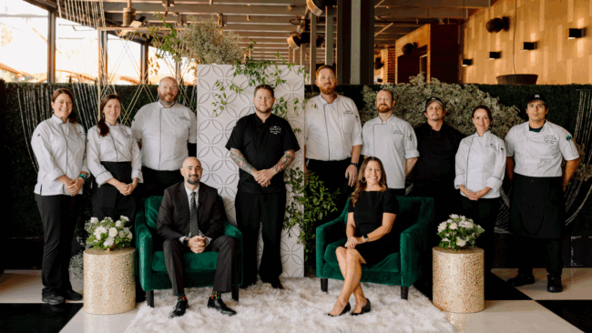 Team Woodlands private dining servers, chefs and event planner posing in a fancy green and white backdrop outside on the patio