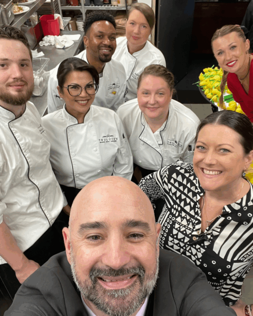 General Manager Joe of The Woodlands taking a selfie style photo with several servers, a manager and host in the background while standing in the kitchen and prepping for a busy shift.