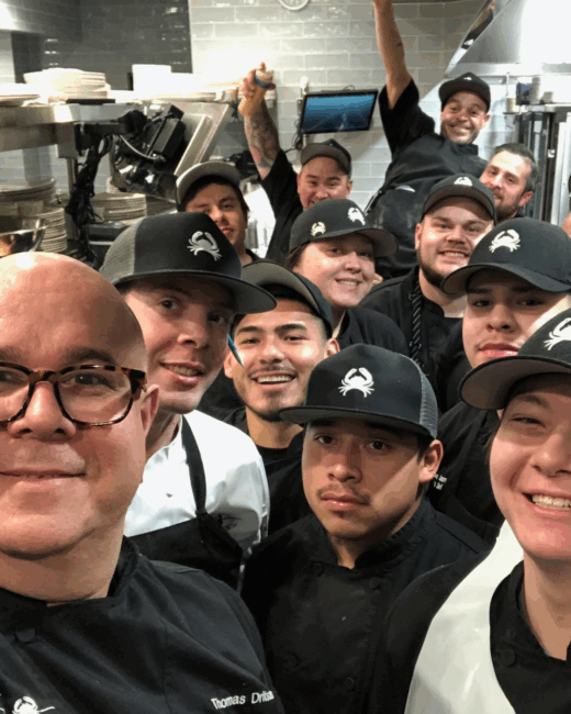 The kitchen team in Plano with Chef Thomas smiling and grouped tightly together getting ready for a busy shift