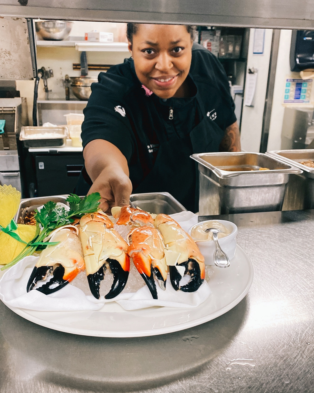 Chef Paigton of Southlake pushing a fresh plate of cracked stone crab claws on ice with mustard sauce through the kitchen window