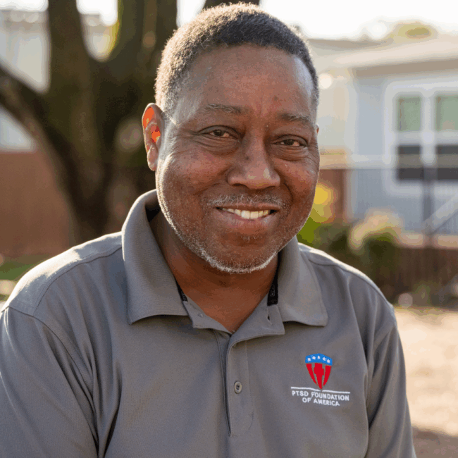 a photo of a PTSD Foundation of America Camp Hope resident in a gray polo shirt standing outside with a tree in the background