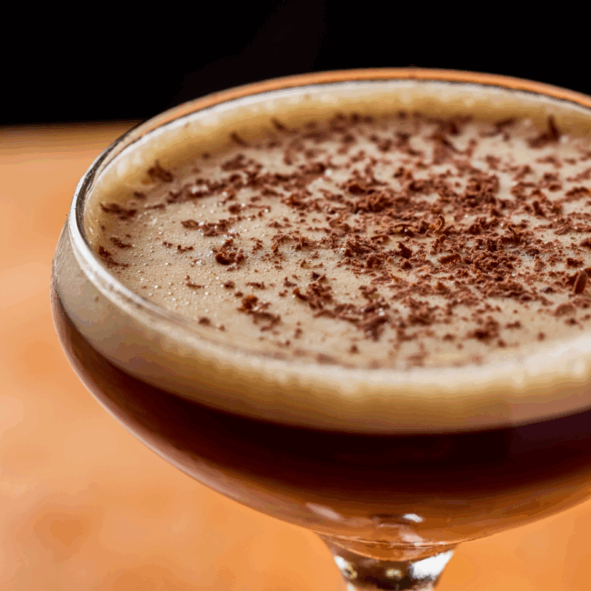 a close up image of an espresso martini in a coupe style glass with a foamy top and shaved chocolate on top