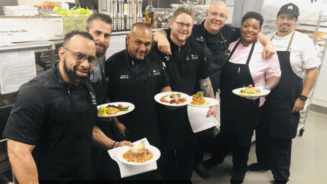 a group shot with Texas executive chefs and corporate chef team standing with entrees in a group and smiling in the kitchen