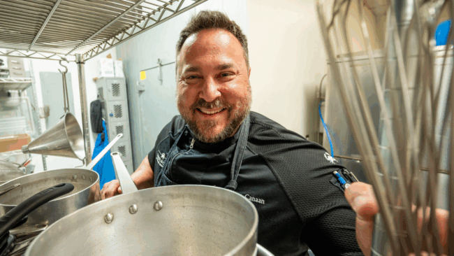 Chef Sammy smiling and looking through a shelf with pots and pans on it at Camp Hope