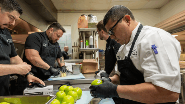 Chef Michael, Chef Sammy, Chef Shane and Chef Misael prepping in the kitchen together, Chef Misael is peeling apples for a salad.