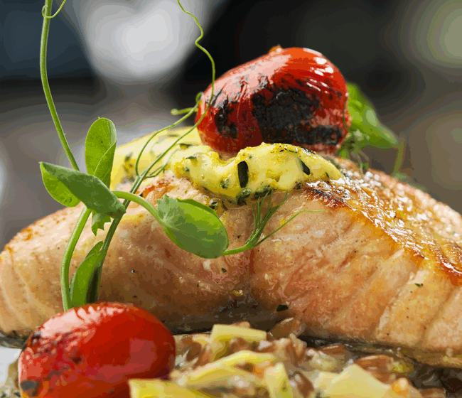 side view of an Ora King Salmon filet with farro & leek fondue, citrus-tarragon butter, blistered tomato and fresh pea tendrils