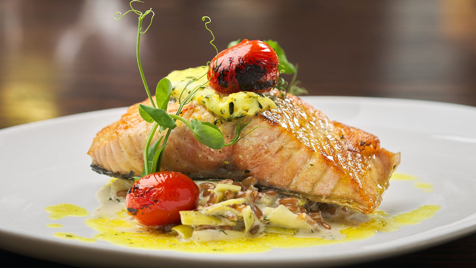 close up shot of Ora King Salmon filet topped with blistered tomato and fresh pea tendrils over farro & leek fondue with citrus-tarragon butter