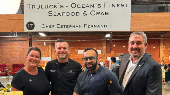 Ryan Studt general manager of Truluck's Dallas with his Dallas teammates from left to right, Monica, Keegan, Chef Estephan standing in front of a sign that says "Truluck's Ocean's Finest Seafood & Crab Chef Estephan Fernandez"