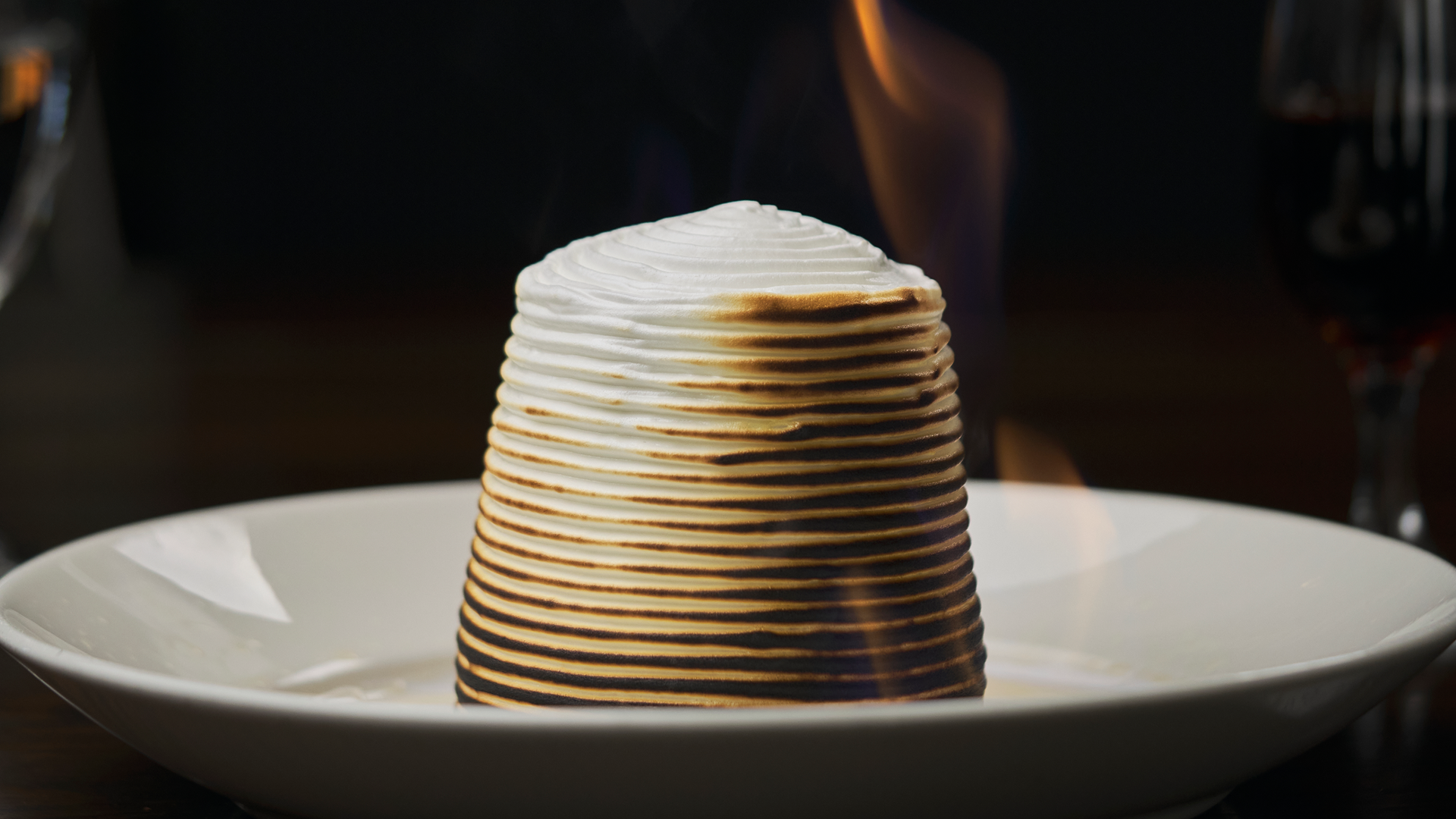 traditional baked Alaska dessert on a white china plate with a creamy meringue that is lit aflame and baked