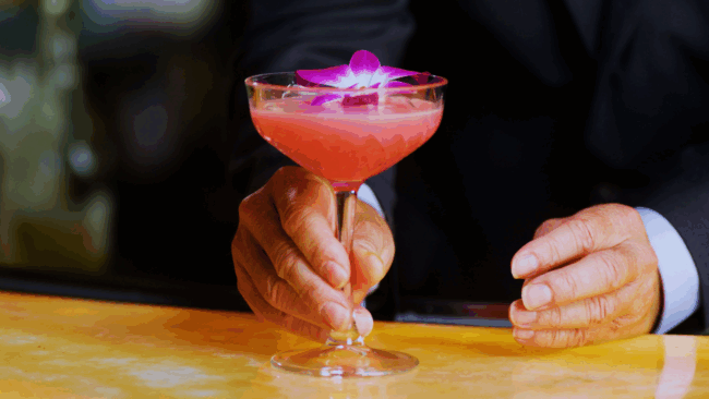 Hibiscus Fresca zero proof cocktail with hibiscus, spiced orange, almond, fresh lemon, fresh lime, and soda water, served over ice.