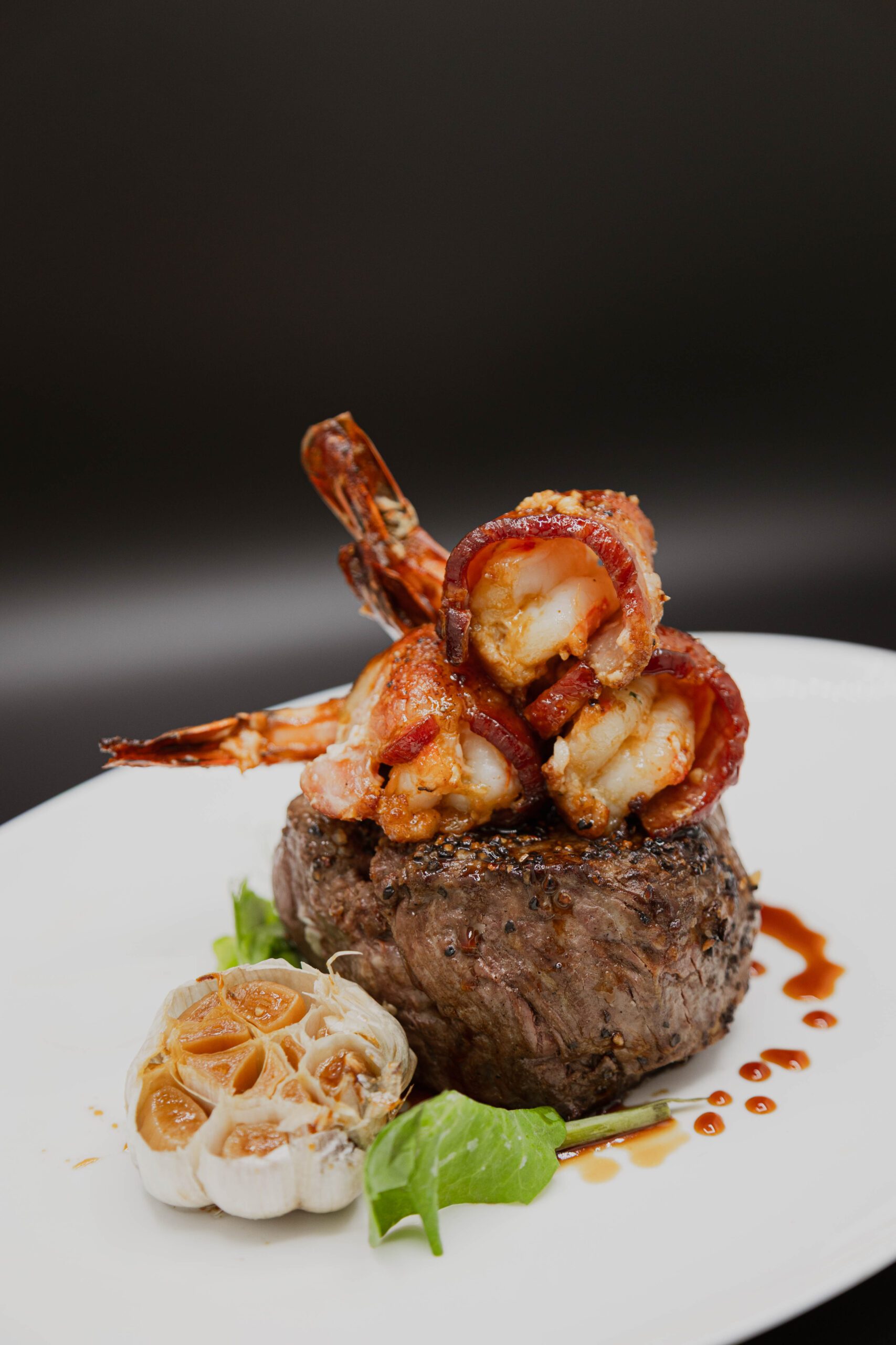 beef tenderloin filet topped with 3 bacon wrapped shrimp with a side of roasted garlic on the side