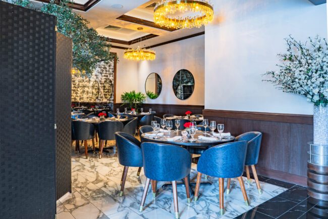 Refined group dining space at Truluck’s featuring navy chairs, chandeliers, and floral décor.