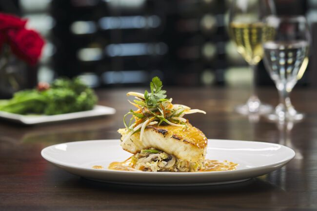 miso glazed seabass atop a bed of crab fried rice with miso glaze and a fresh cucumber slaw on a white china plate