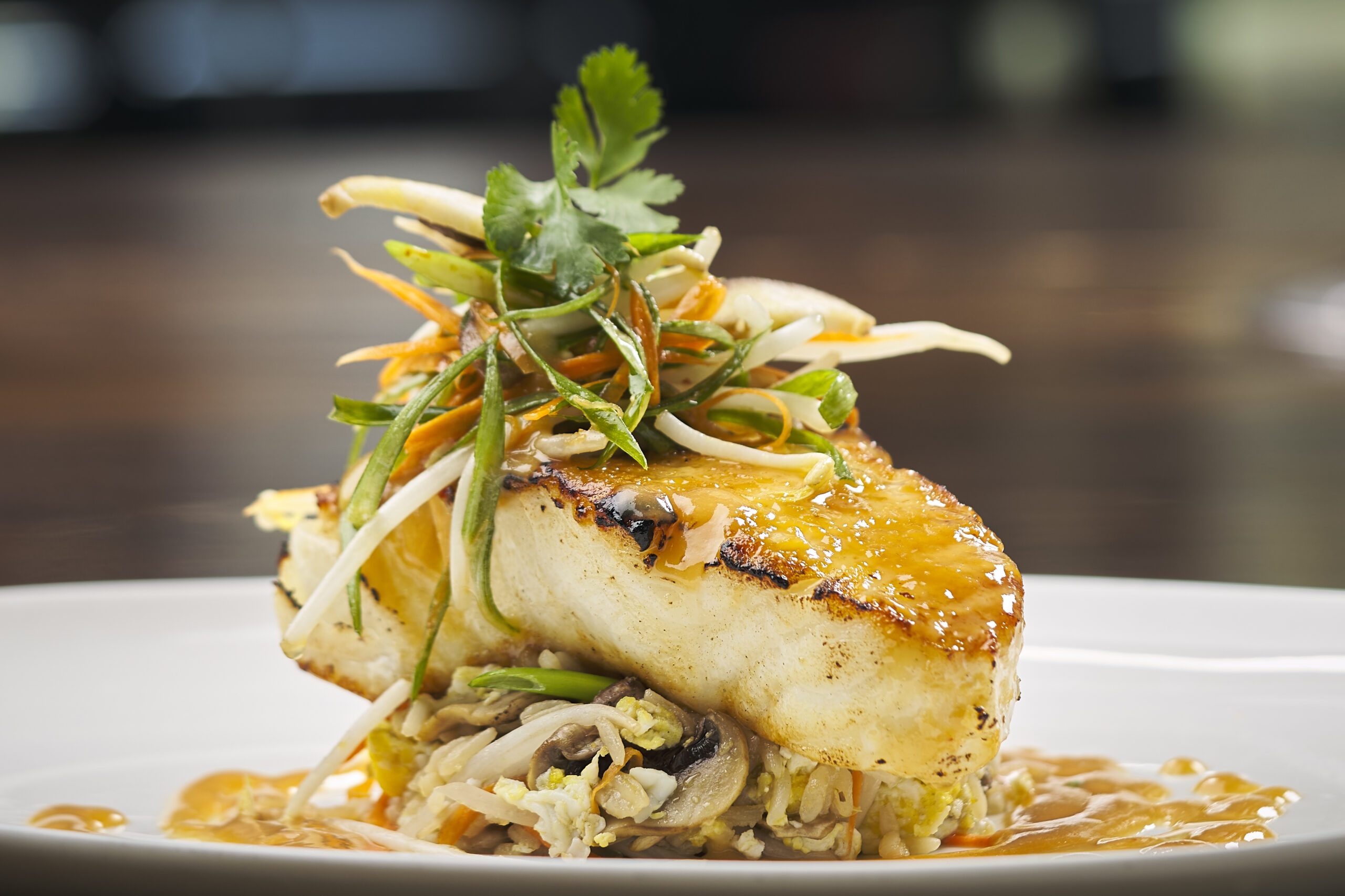miso glazed seabass atop a bed of crab fried rice with miso glaze and a fresh cucumber slaw on a white china plate