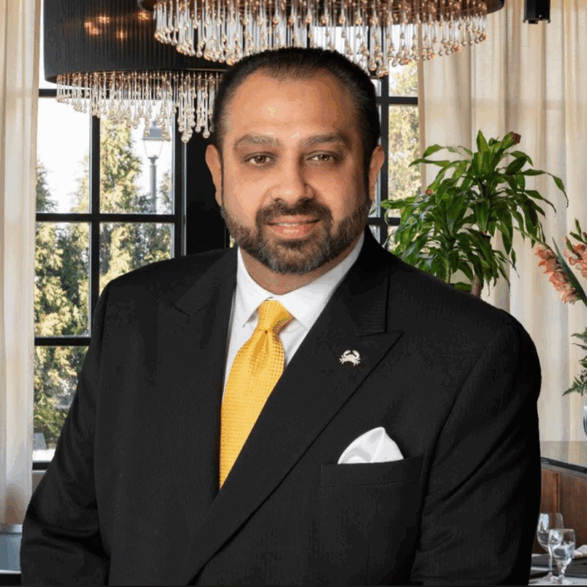 Blake Goldie standing confidently in Truluck's Rosemont restaurant dining room, wearing a black suit with a gold tie and pocket square