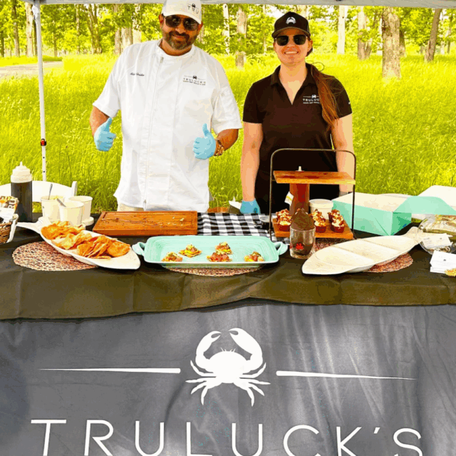 Blake Goldie of Truluck's Rosemont with a team member smiling while serving food at a golf tournament, featuring chef-prepared appetizers at an outdoor event
