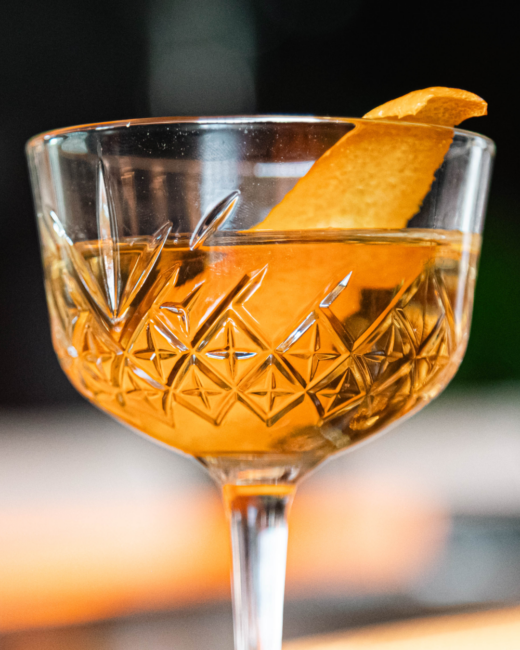 El Tesoro Tiny Tini cocktail served in a cut-crystal stemmed glass, garnished with an orange peel.