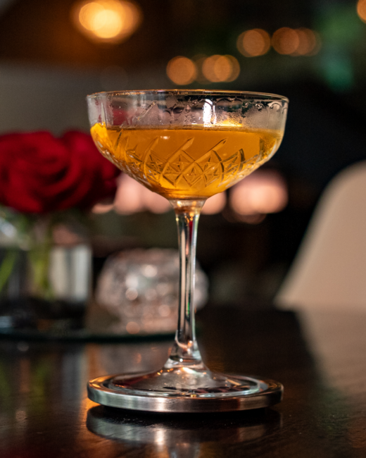 El Tesoro martini cocktail glowing amber in a vintage crystal coupe with an orange peel garnish.