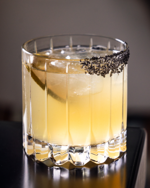 A refined El Tesoro single-barrel margarita cocktail served on the rocks in a cut crystal glass with a dramatic black salt rim.