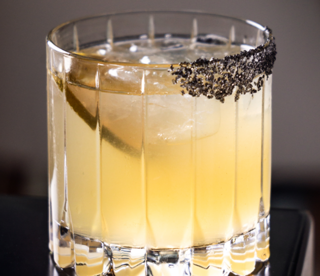 A refined El Tesoro single-barrel margarita cocktail served on the rocks in a cut crystal glass with a dramatic black salt rim.