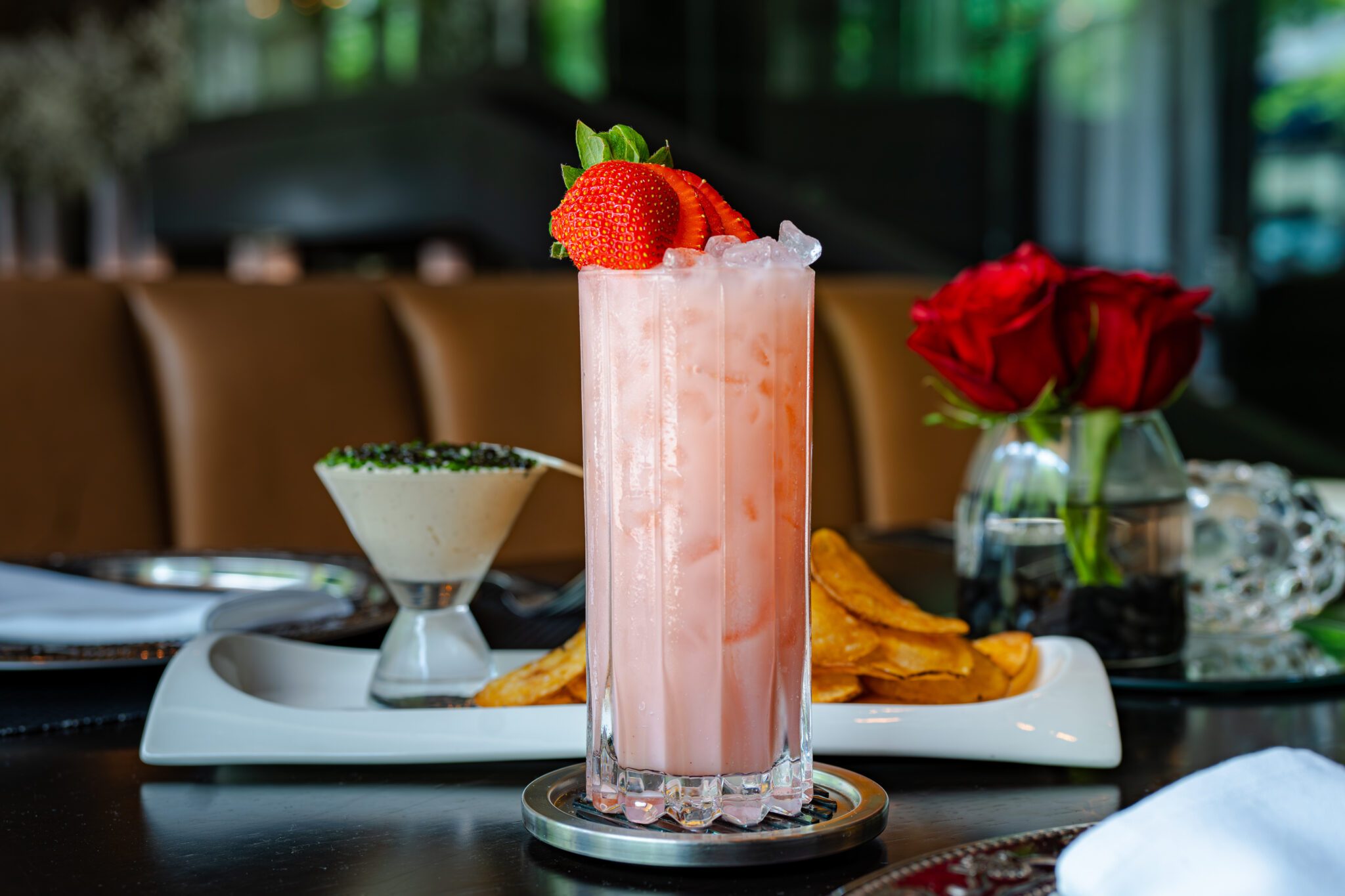 Berry Patch non-alcoholic cocktail served over ice in a tall glass, garnished with fresh sliced strawberries, set beside chips and guacamole on a dark dining table with natural light from nearby windows.